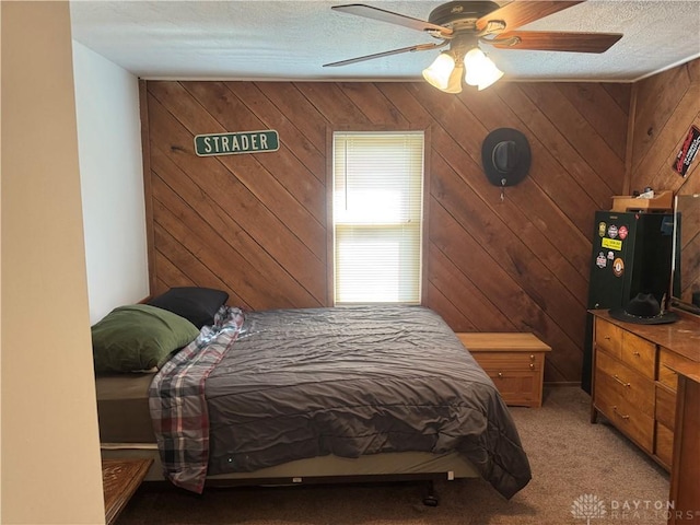 bedroom with a ceiling fan, wooden walls, light colored carpet, and a textured ceiling