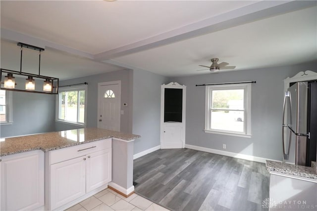 kitchen featuring light stone counters, a healthy amount of sunlight, white cabinets, and freestanding refrigerator