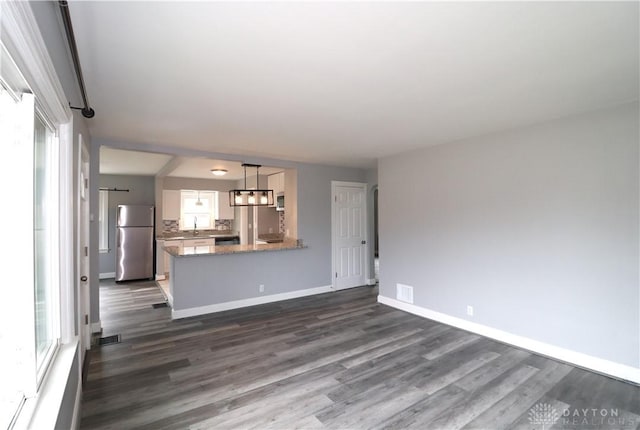 unfurnished living room with baseboards, plenty of natural light, and dark wood finished floors