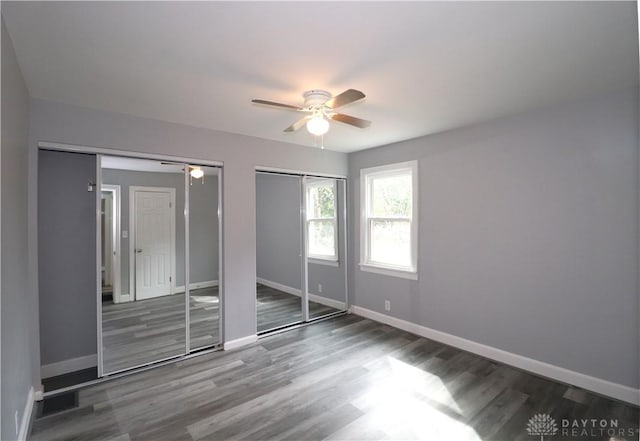 unfurnished bedroom with visible vents, two closets, wood finished floors, baseboards, and ceiling fan