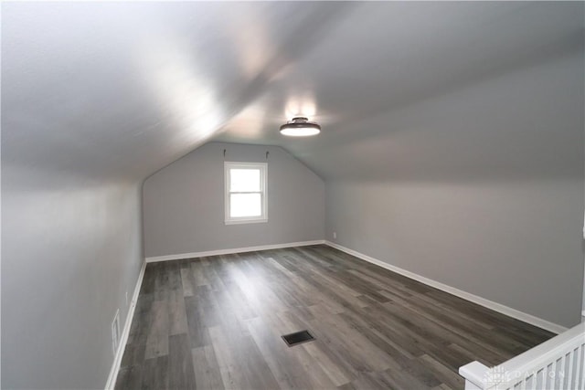 additional living space featuring visible vents, baseboards, dark wood-type flooring, and vaulted ceiling