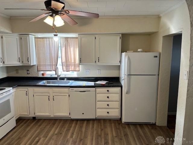 kitchen featuring dark countertops, dark wood finished floors, ornamental molding, white appliances, and a sink