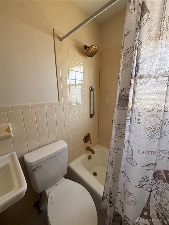 full bath featuring a wainscoted wall, toilet, shower / bath combination with curtain, tile walls, and a sink