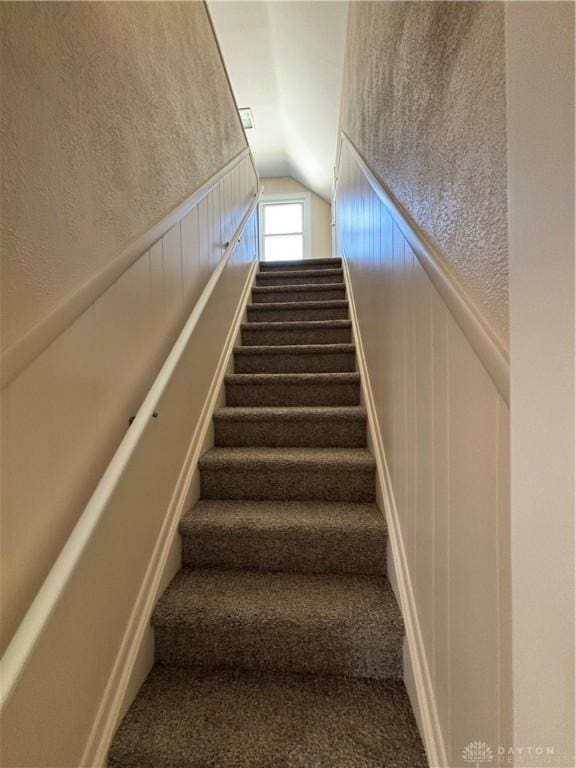 stairway featuring a decorative wall, a wainscoted wall, carpet, and vaulted ceiling