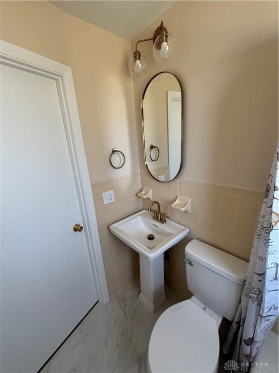 bathroom with a wainscoted wall, tile walls, toilet, and marble finish floor