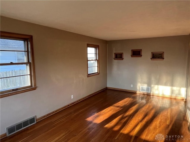 empty room with dark wood finished floors, baseboards, and visible vents