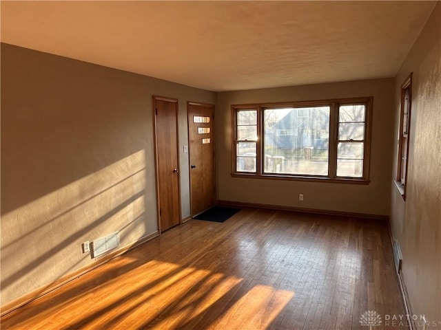 empty room featuring hardwood / wood-style flooring, visible vents, and baseboards