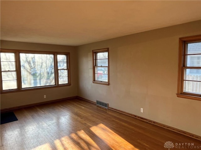 empty room with wood finished floors, visible vents, and baseboards