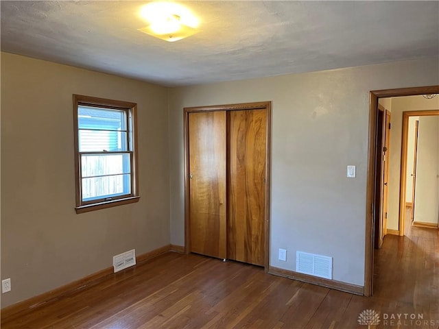 unfurnished bedroom featuring a closet, visible vents, baseboards, and wood finished floors