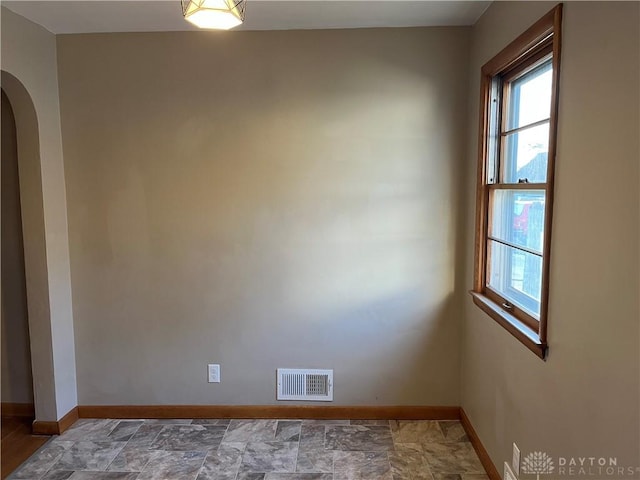 spare room with arched walkways, visible vents, stone finish floor, and baseboards