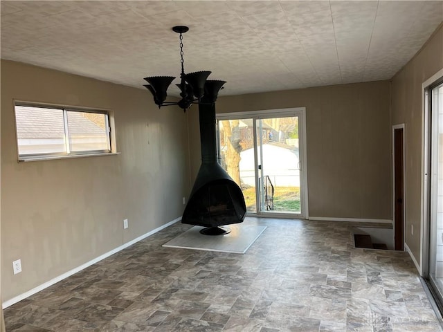 unfurnished living room with stone finish flooring, baseboards, an inviting chandelier, and a wood stove