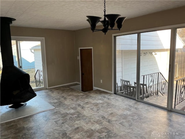 interior space with baseboards, a wood stove, stone finish floor, a textured ceiling, and a notable chandelier