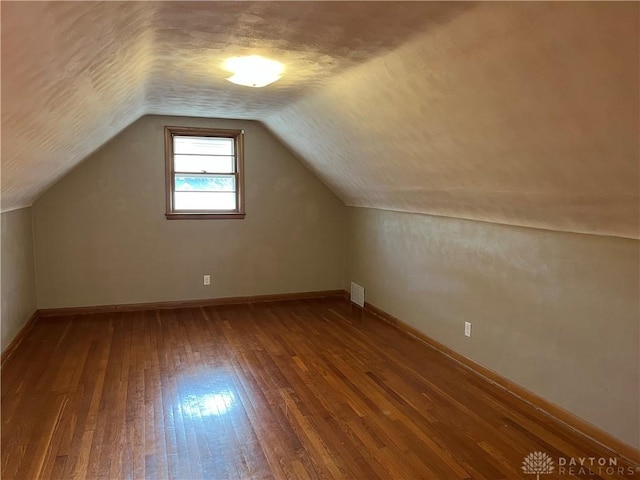 additional living space with baseboards, visible vents, vaulted ceiling, wood-type flooring, and a textured ceiling