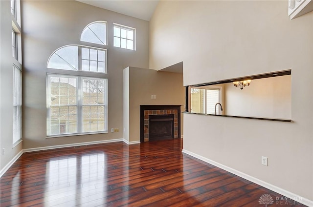 unfurnished living room featuring baseboards, a tile fireplace, a high ceiling, a notable chandelier, and wood-type flooring