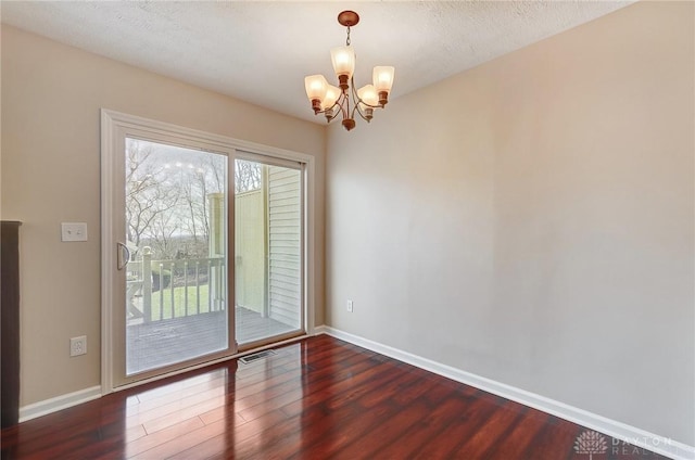 unfurnished room featuring wood finished floors, visible vents, baseboards, a textured ceiling, and a notable chandelier