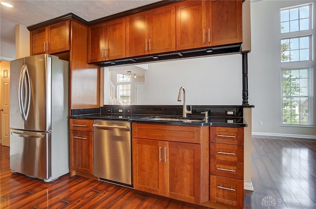 kitchen with baseboards, brown cabinets, appliances with stainless steel finishes, dark wood-style floors, and a sink