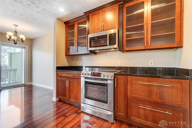 kitchen with dark countertops, dark wood-style floors, appliances with stainless steel finishes, an inviting chandelier, and brown cabinetry