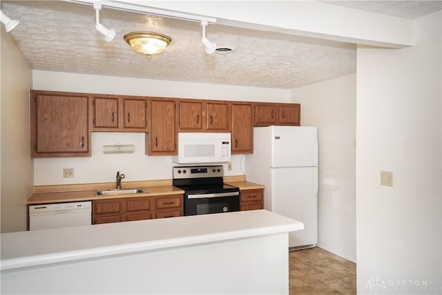 kitchen featuring white appliances, brown cabinetry, a sink, light countertops, and a textured ceiling