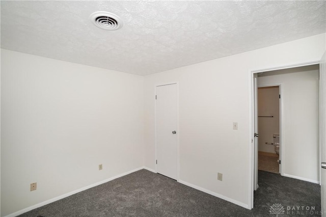 unfurnished bedroom featuring visible vents, a textured ceiling, dark carpet, a closet, and baseboards