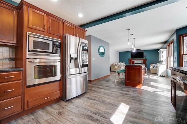 kitchen with backsplash, ceiling fan, open floor plan, appliances with stainless steel finishes, and brown cabinetry