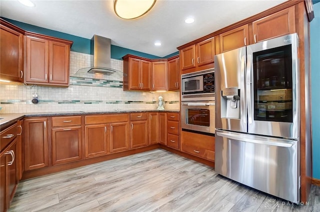 kitchen with brown cabinets, light wood-style flooring, light stone counters, appliances with stainless steel finishes, and wall chimney range hood