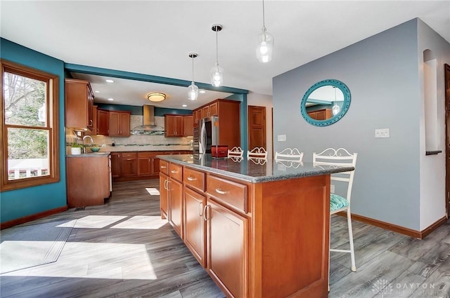 kitchen with a breakfast bar area, brown cabinetry, smart refrigerator, wall chimney range hood, and backsplash