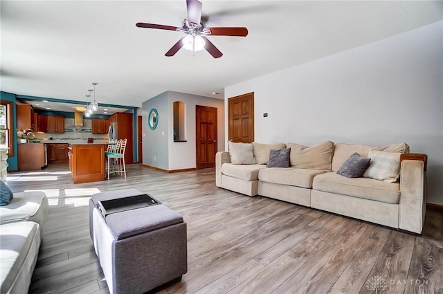 living area featuring light wood-style flooring, a ceiling fan, and baseboards