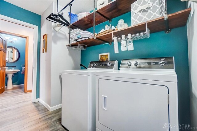 washroom with a sink, wood finished floors, washing machine and dryer, baseboards, and laundry area