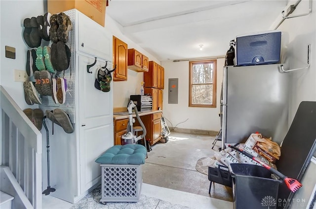 kitchen featuring concrete flooring, light countertops, electric panel, brown cabinets, and freestanding refrigerator