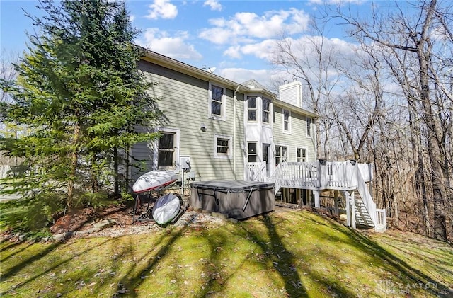 rear view of property featuring a lawn, a deck, stairway, a chimney, and a hot tub