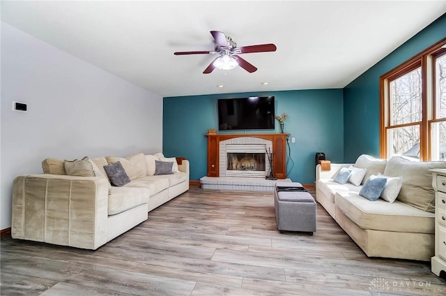 living area featuring light wood-style floors, ceiling fan, and a fireplace