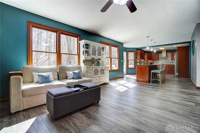 living area featuring a healthy amount of sunlight, baseboards, dark wood-type flooring, and a ceiling fan