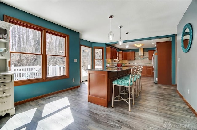 kitchen featuring a kitchen bar, wall chimney exhaust hood, wood finished floors, and freestanding refrigerator