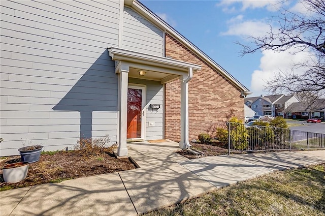 doorway to property featuring brick siding and fence