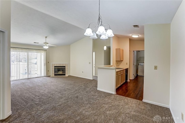 interior space featuring a tiled fireplace, decorative light fixtures, dark carpet, lofted ceiling, and ceiling fan with notable chandelier