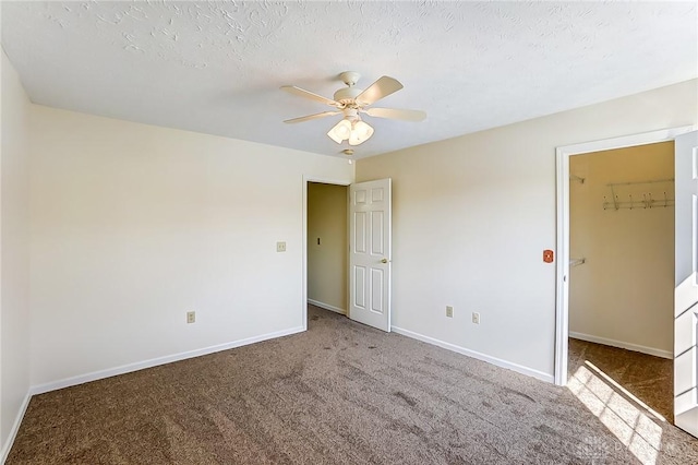 unfurnished bedroom featuring a spacious closet, a textured ceiling, carpet, and baseboards