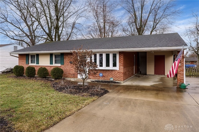 ranch-style home featuring brick siding, a front yard, roof with shingles, a carport, and driveway