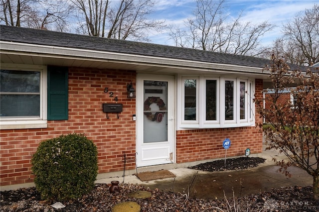 doorway to property featuring brick siding and a shingled roof