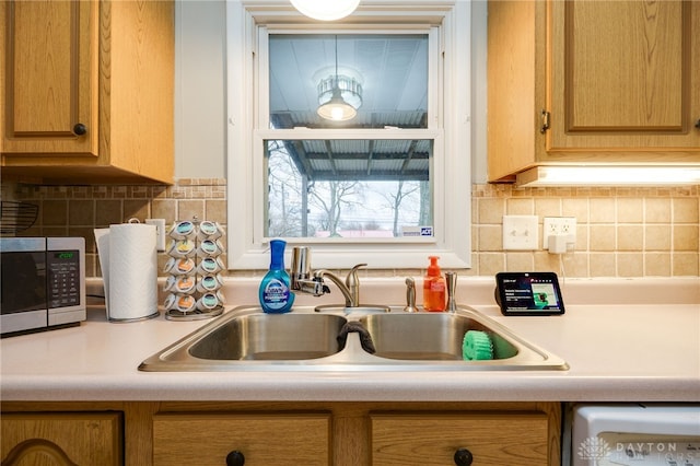 kitchen with a sink, stainless steel microwave, decorative backsplash, and light countertops