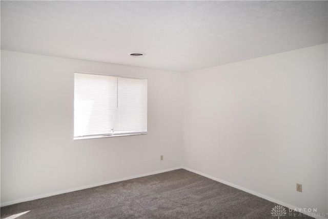 spare room with visible vents, baseboards, and dark carpet