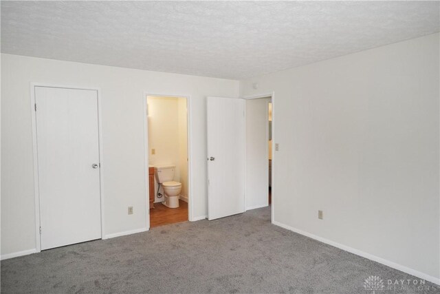 unfurnished bedroom featuring connected bathroom, a textured ceiling, baseboards, and carpet floors