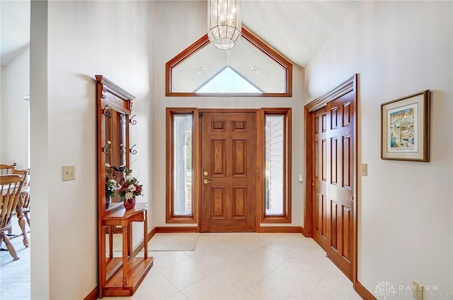 foyer entrance with light tile patterned floors, baseboards, high vaulted ceiling, and an inviting chandelier