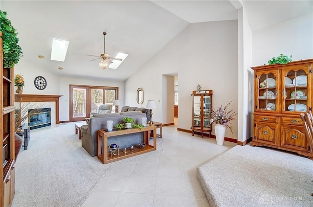 living area featuring high vaulted ceiling, light tile patterned flooring, a skylight, a fireplace, and baseboards