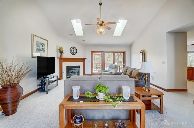 living room featuring a glass covered fireplace, a skylight, baseboards, and high vaulted ceiling