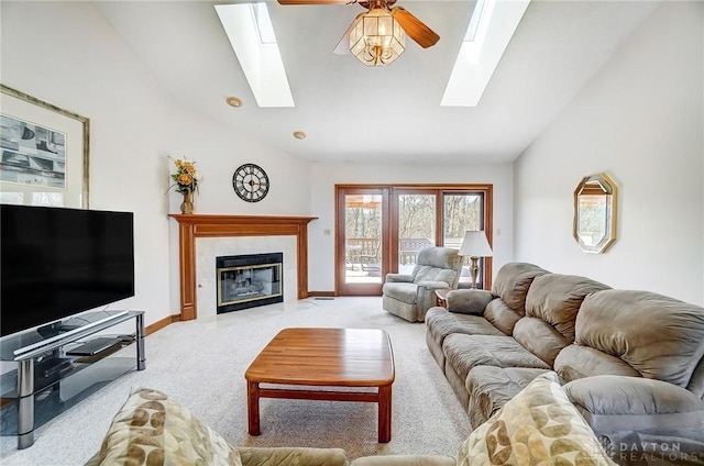 living room featuring a ceiling fan, a skylight, a fireplace, baseboards, and light colored carpet