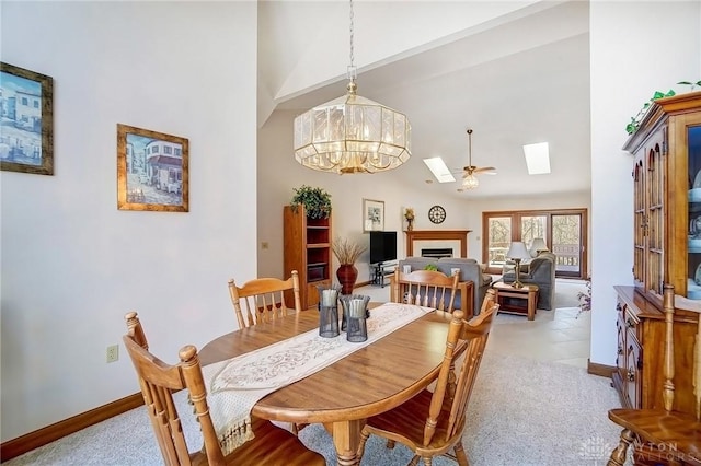 dining space with baseboards, a fireplace, a skylight, an inviting chandelier, and high vaulted ceiling