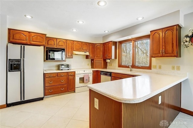 kitchen with white appliances, a peninsula, a sink, light countertops, and under cabinet range hood