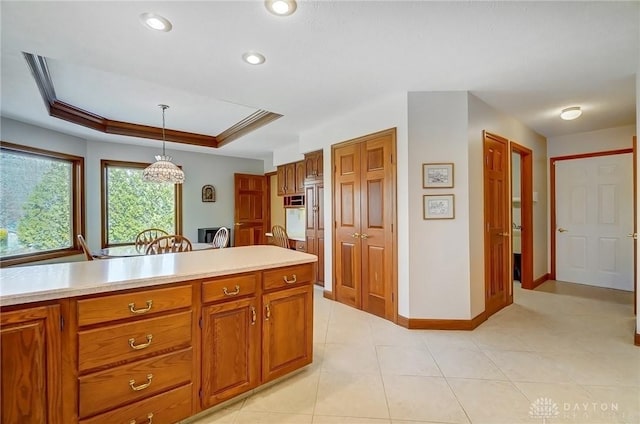 kitchen featuring light tile patterned floors, brown cabinetry, a tray ceiling, light countertops, and pendant lighting