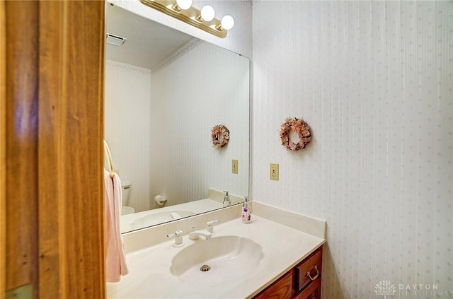 half bathroom with vanity, toilet, and wallpapered walls