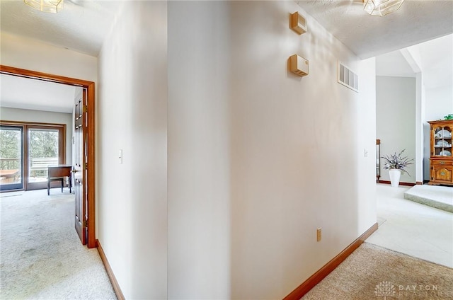 corridor with baseboards, visible vents, and light carpet